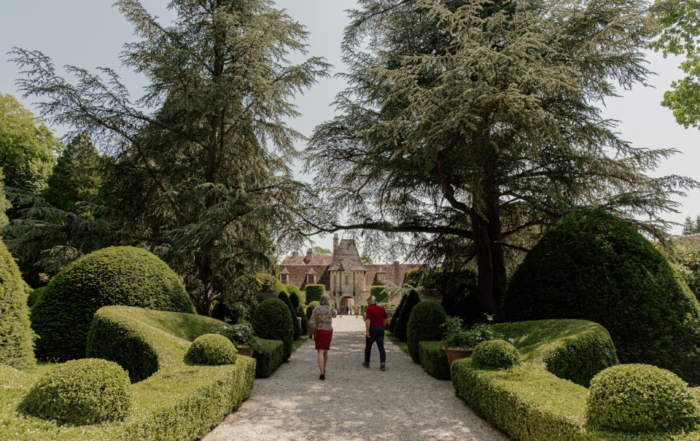 Allée bordée d'arbres menant au Château de Boutemont, entourée de haies sculptées.