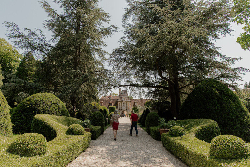 Allée bordée d'arbres menant au Château de Boutemont, entourée de haies sculptées.