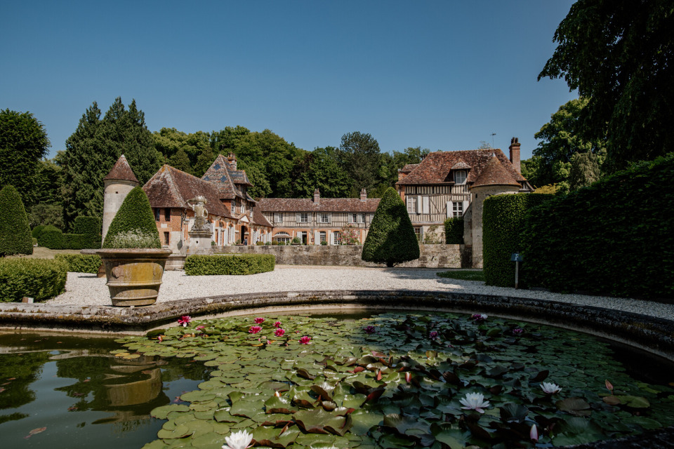 Une vue charmante des jardins et du château de Boutemont, entourés de verdure et d'un étang fleuri.