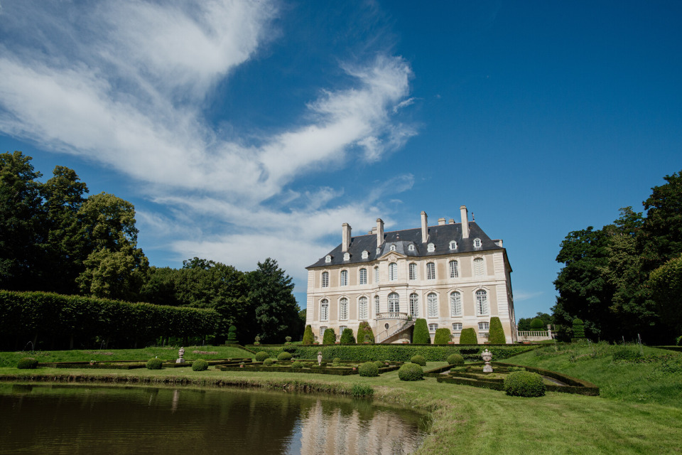 Vue magnifique des jardins du Château de Vendeuvre avec des haies sculptées et un ciel dégagé.