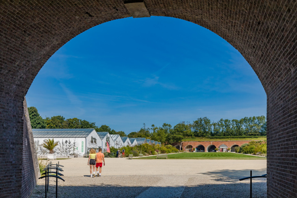 Vue à travers une arche sur les jardins suspendus du Havre avec des serres modernes et un ciel bleu.