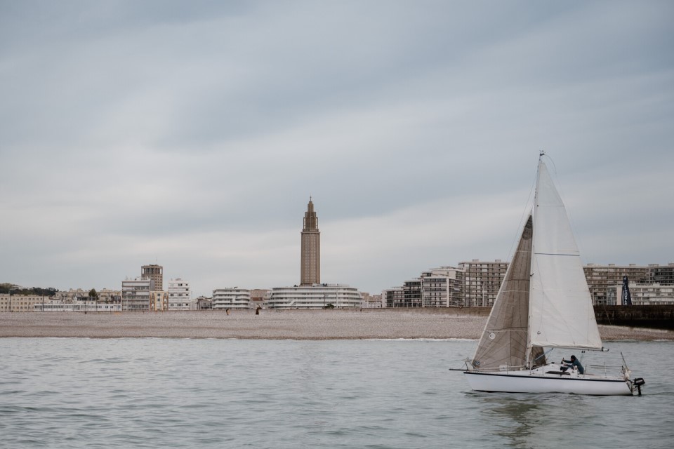 Voilier naviguant au large du Havre avec la ville en arrière-plan.